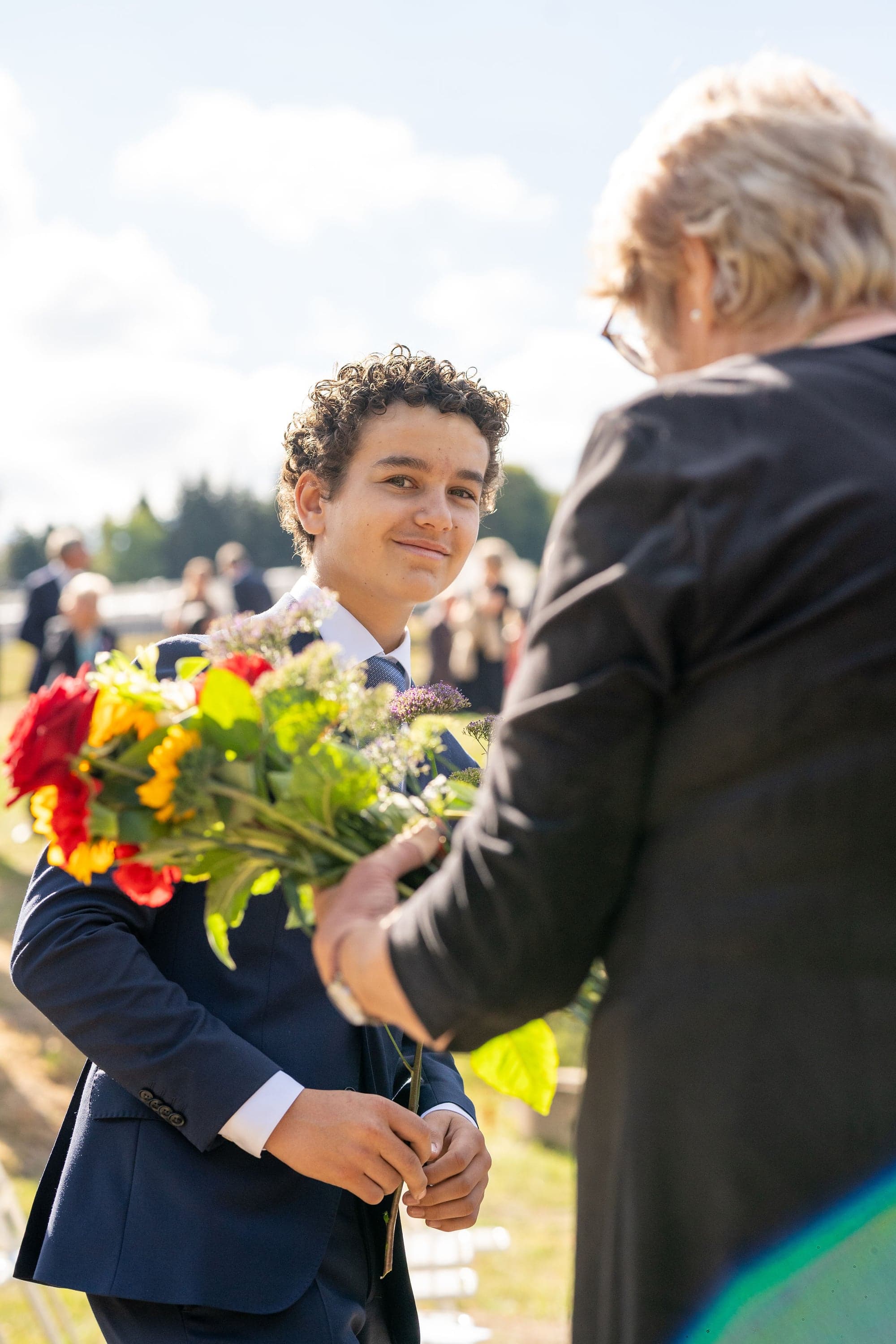 En av de unge i følget mottar en blomst for å legge den ned ved askegraven