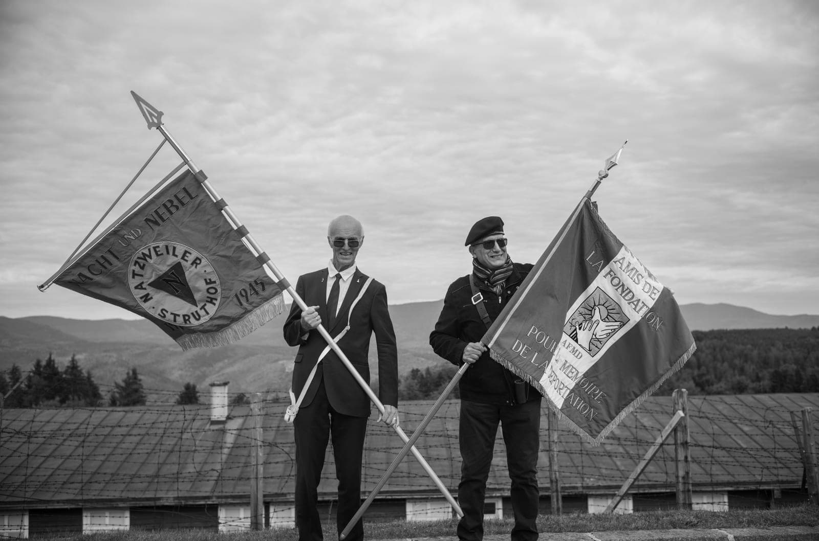 DNNDs fane og fanen til den franske deportasjonsminnestiftelsen, båret side om side foran krematoriebygningen i leiren